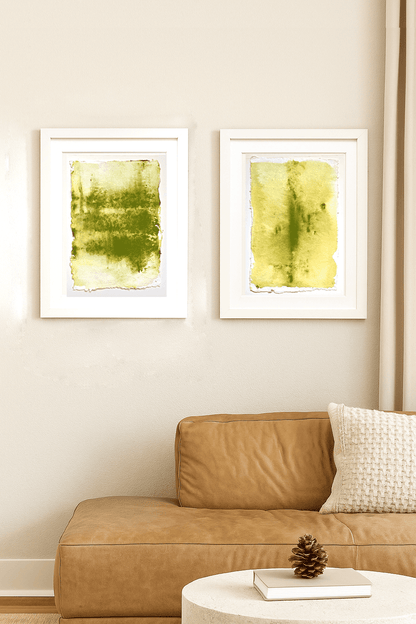 Two framed Verdant Memory paintings by Carrie Bergey above a tan leather sofa, blending fine art with cozy living room decor.